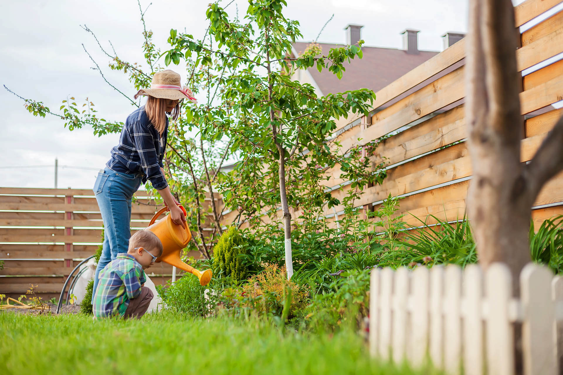 Mutter und Tochter im Garten vor Holzzaun bei Doppelhaushäfte